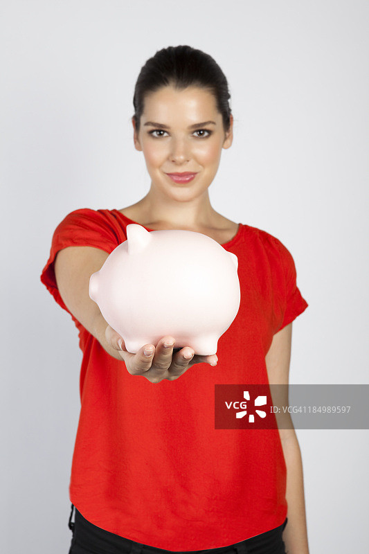 在灰色的背景下，年轻的女人拿着存钱罐图片素材