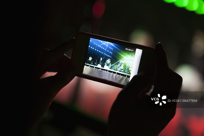 年轻女子在一个室内音乐会用她的智能手机拍照，近距离在手图片素材