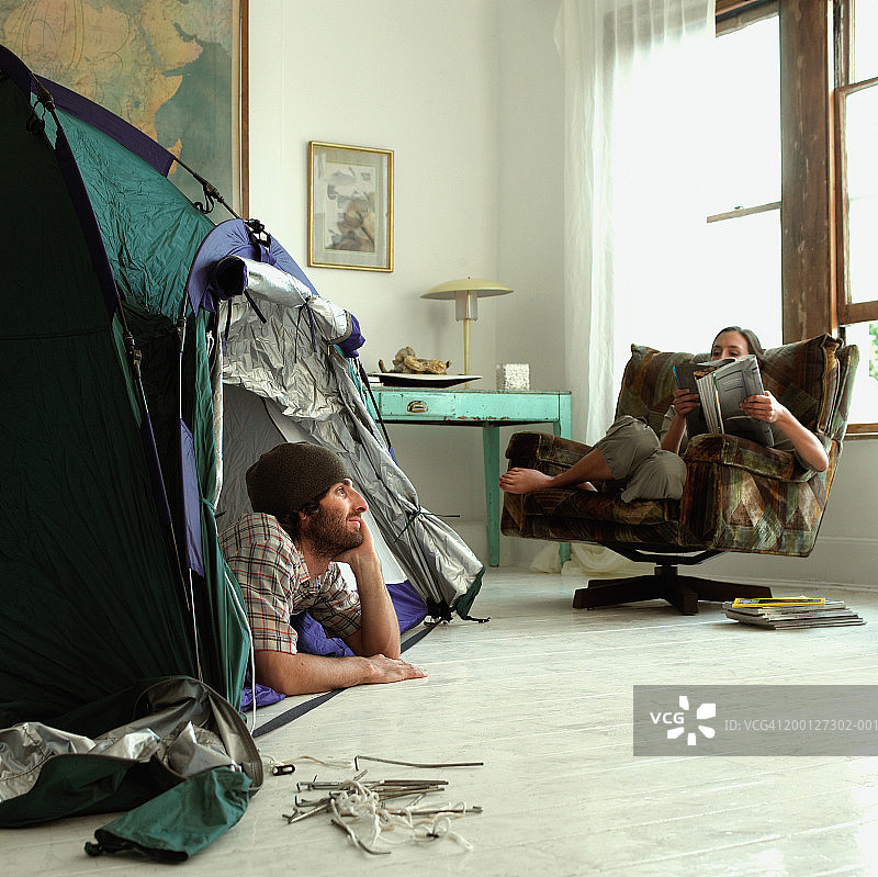 男人躺在客厅搭的帐篷里，女人坐在扶手椅里图片素材