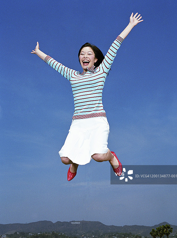 女子在空中跳跃，双臂伸展，肖像，低角度图片素材