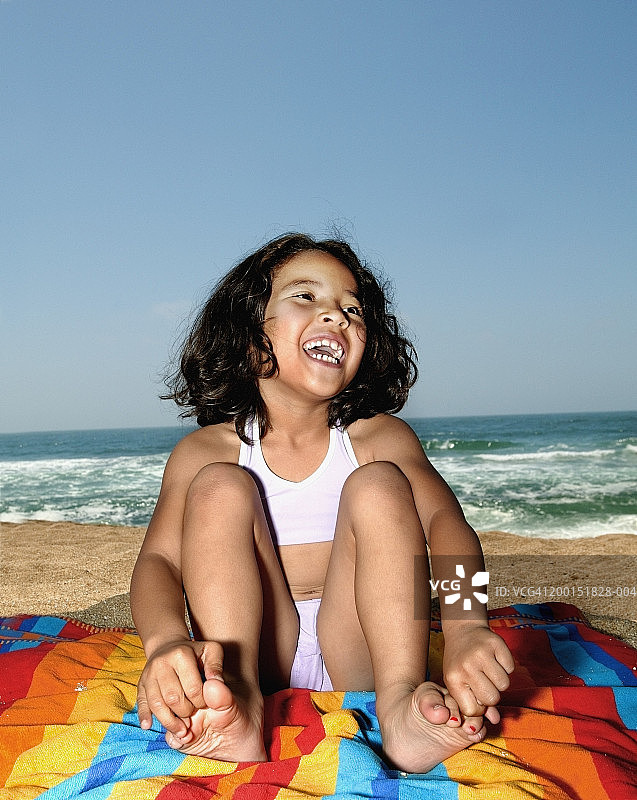 女孩(6-8)坐在沙滩浴巾上，笑着图片素材