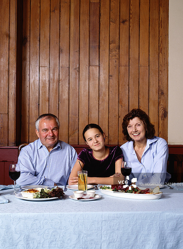 成熟的夫妇和十几岁的女孩(13-15岁)在桌子上，微笑，肖像图片素材
