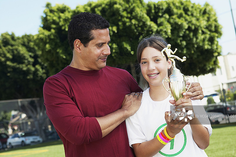 父亲微笑的女儿(11-13)拿着足球奖杯，肖像图片素材