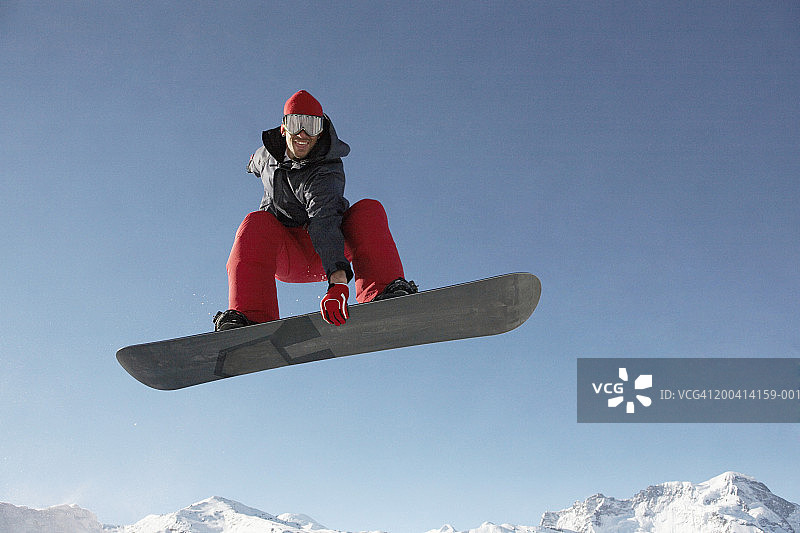 男子在滑雪板上表演跳跃，微笑，低角度观看图片素材