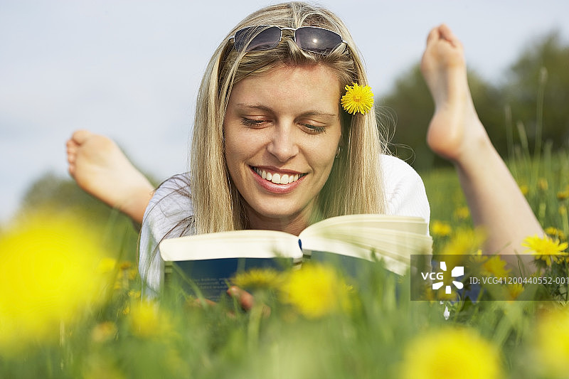 年轻女子躺在草地上看书，面带微笑图片素材