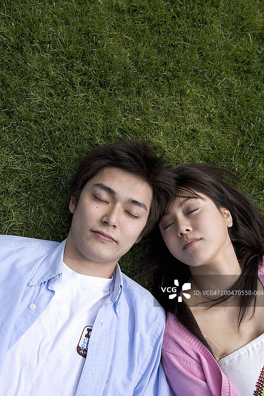 年轻的男男女女躺在草地上，闭着眼睛，俯视图片素材