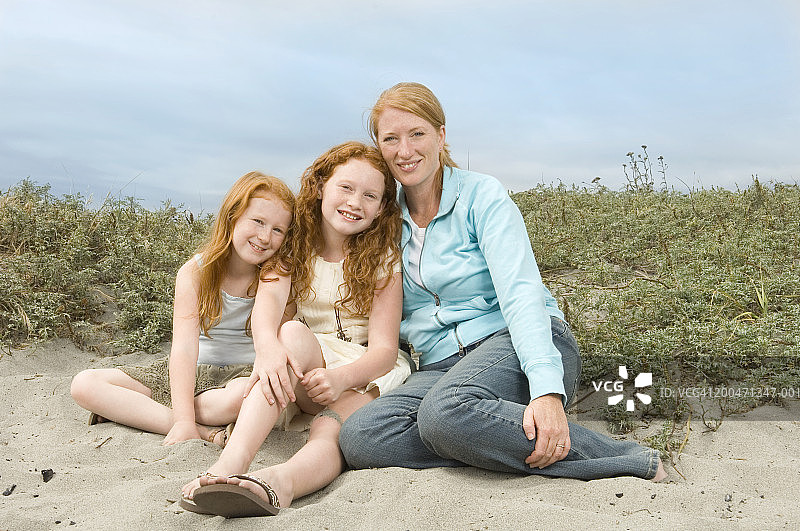 母亲和两个女儿(7-10岁)坐在海滩上，人像图片素材