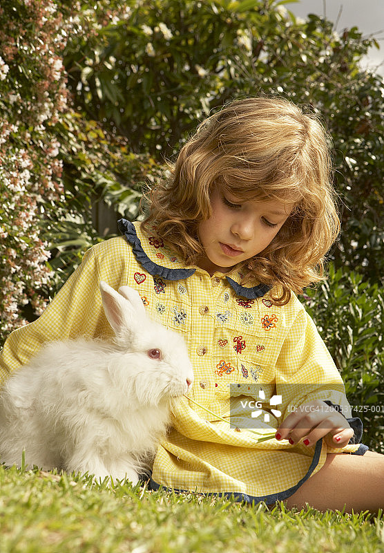 女孩(6-8)和宠物兔子坐在草地上图片素材
