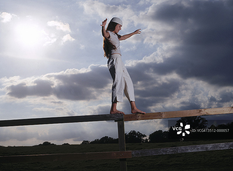 女孩在木栅栏上保持平衡图片素材