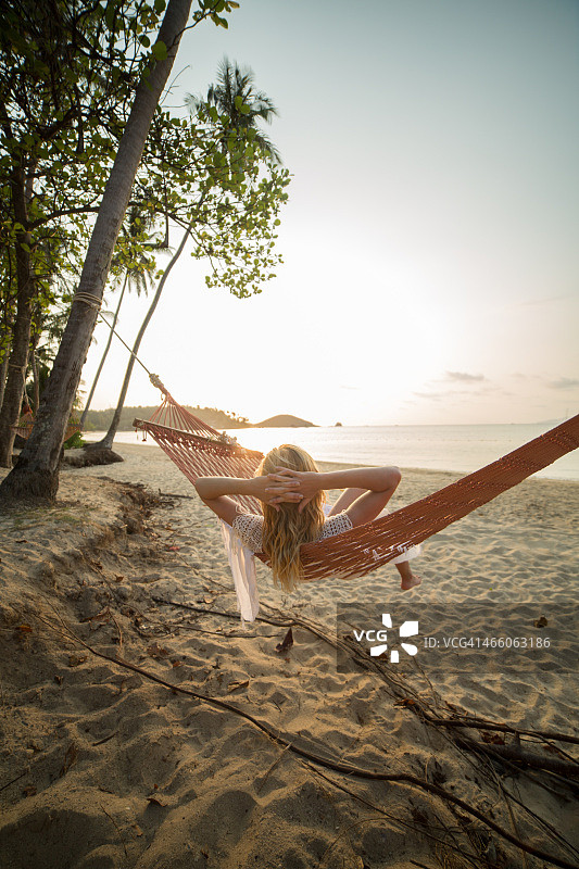 女人在热带海滩上躺在吊床上-日落图片素材