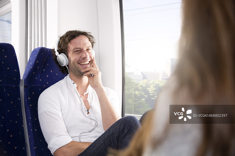 一名男子戴着耳机在火车上对一名女子微笑图片素材