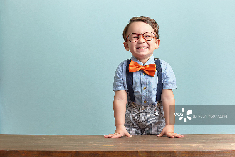 小男孩面带微笑，系着橙色的领结，戴着眼镜图片素材