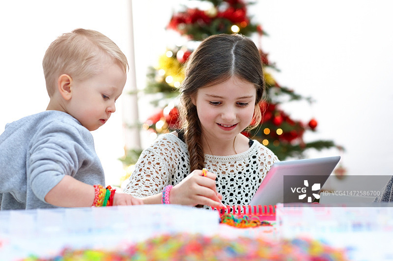 两个小孩一边制作织布机带一边使用数码平板电脑图片素材