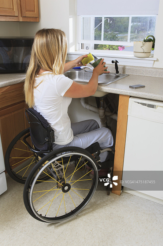 有脊髓损伤的女人在她能到的厨房里洗盘子图片素材
