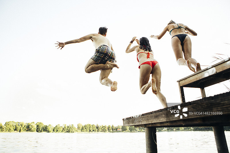 夏日:三个年轻人从防波堤跳入湖中图片素材