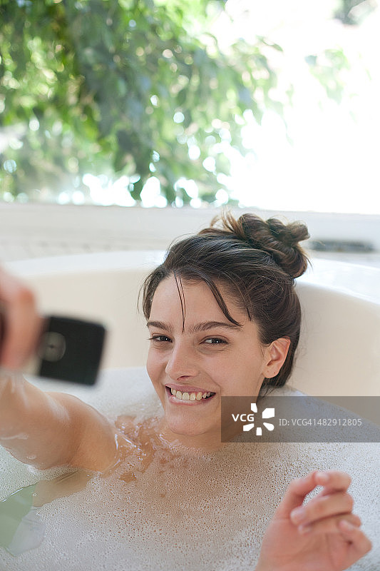 女人放松在泡泡浴中使用手机和微笑图片素材