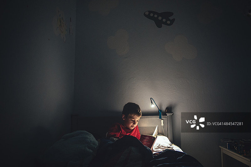 男孩拿着台灯在床上看书图片素材