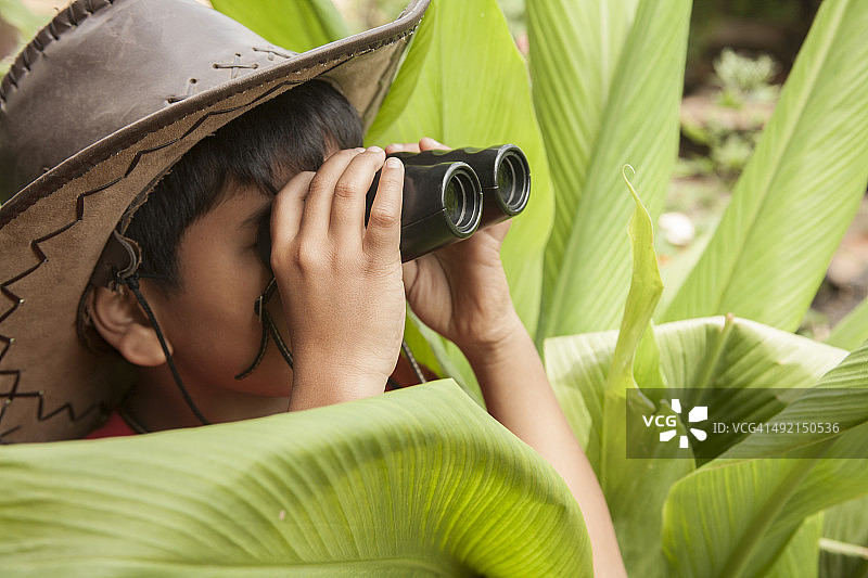 热带气候下的小男孩用双筒望远镜进行户外探险。图片素材
