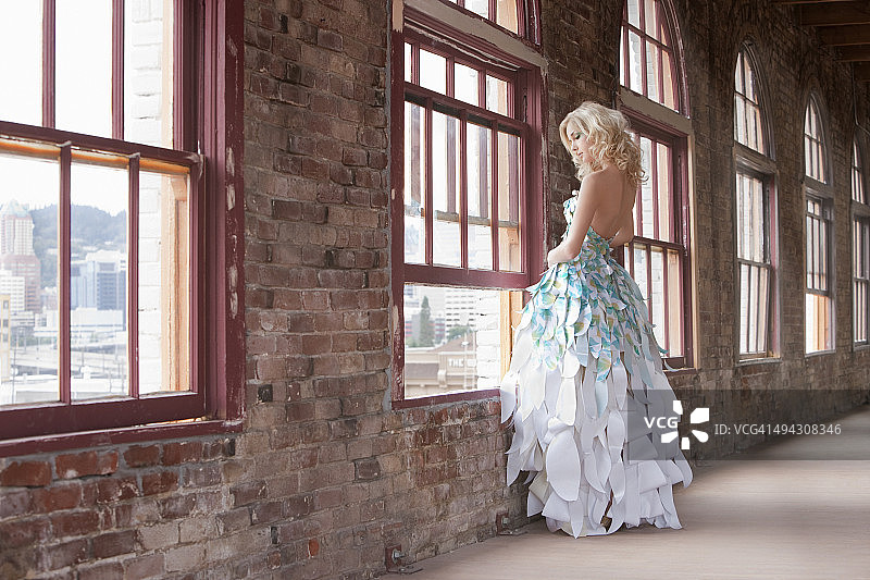 穿着纸裙的女孩站在窗前看着窗外图片素材