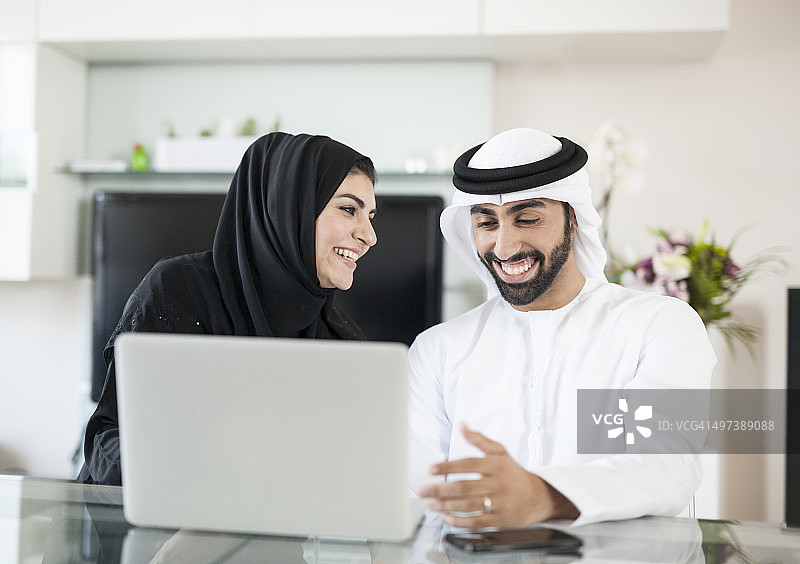 快乐的阿拉伯夫妇花时间在家里使用设备图片素材