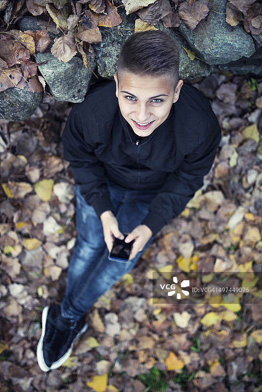 微笑的少年躺在秋叶和使用智能手机图片素材