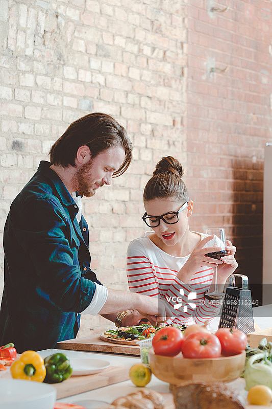 一对夫妇在现代化的厨房里准备披萨，喝着葡萄酒图片素材