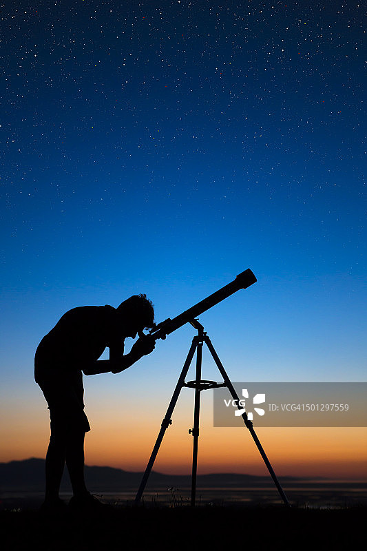 男孩在一个晴朗的夜晚通过望远镜看图片素材