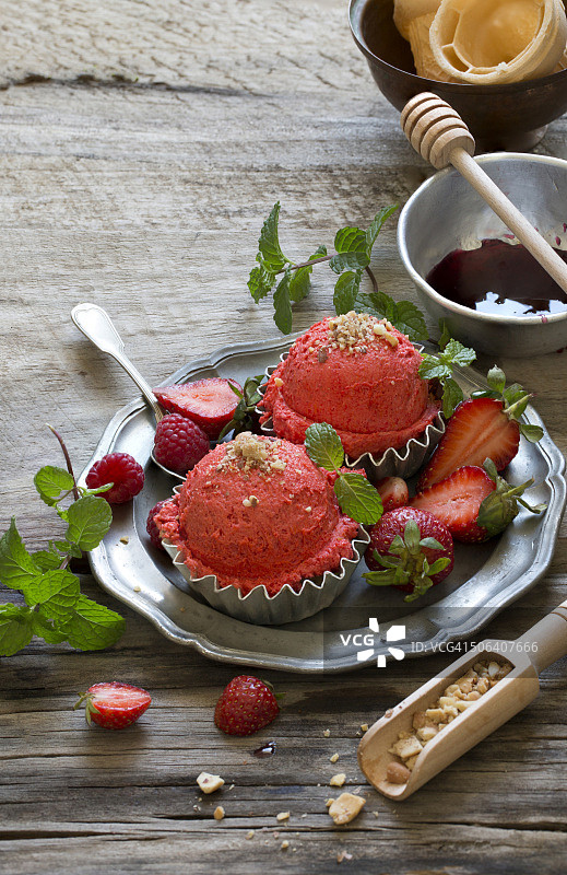 草莓冰淇淋球，新鲜浆果和薄荷叶和草莓糖浆在穆迪乡村木制桌面上。图片素材
