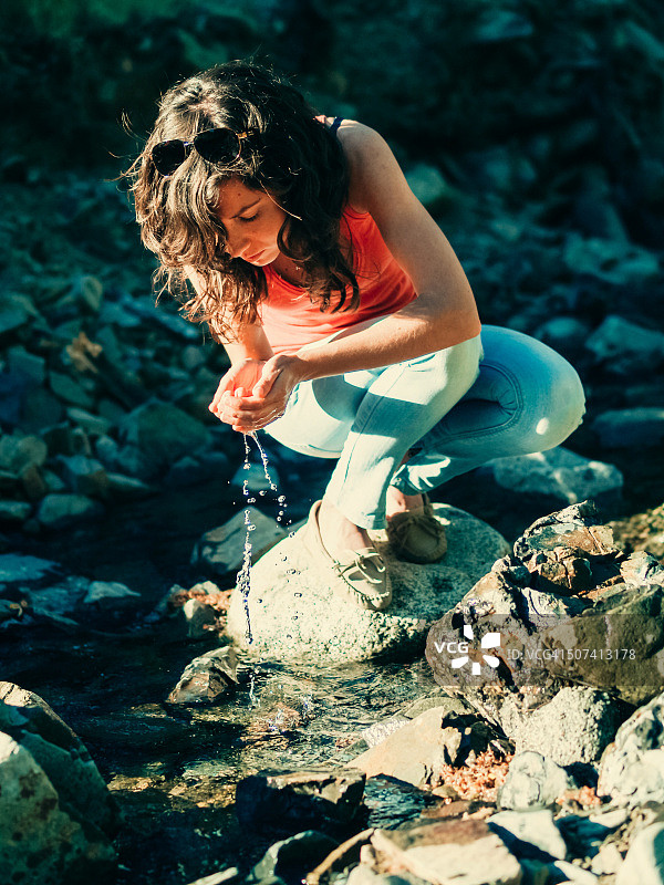 在小溪的岩石上蹲伏着漂亮的女人拿着水图片素材