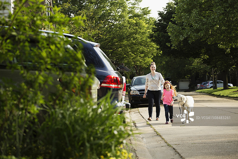 白人母亲和女儿在郊区的街道遛狗图片素材