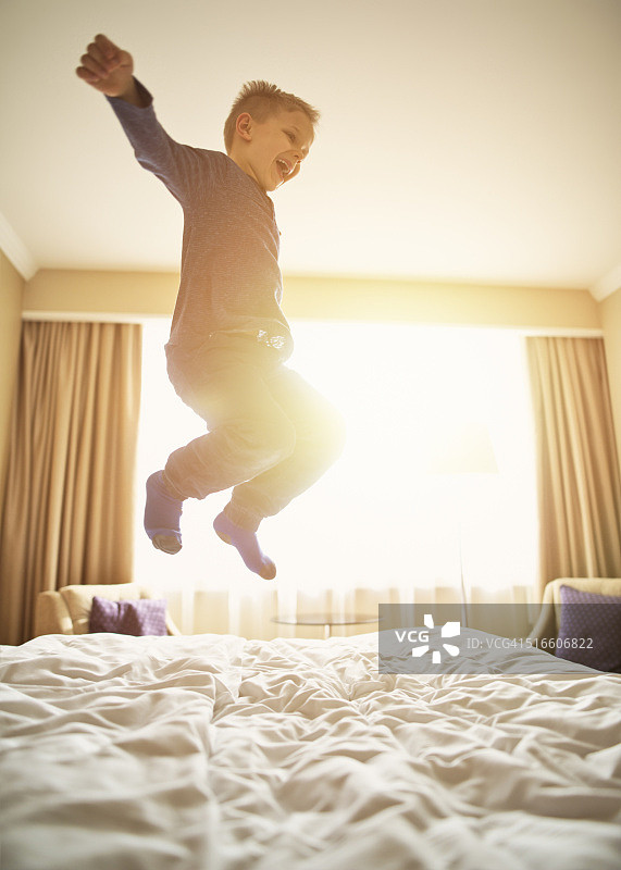 小男孩在床上高兴地在半空中跳跃。图片素材