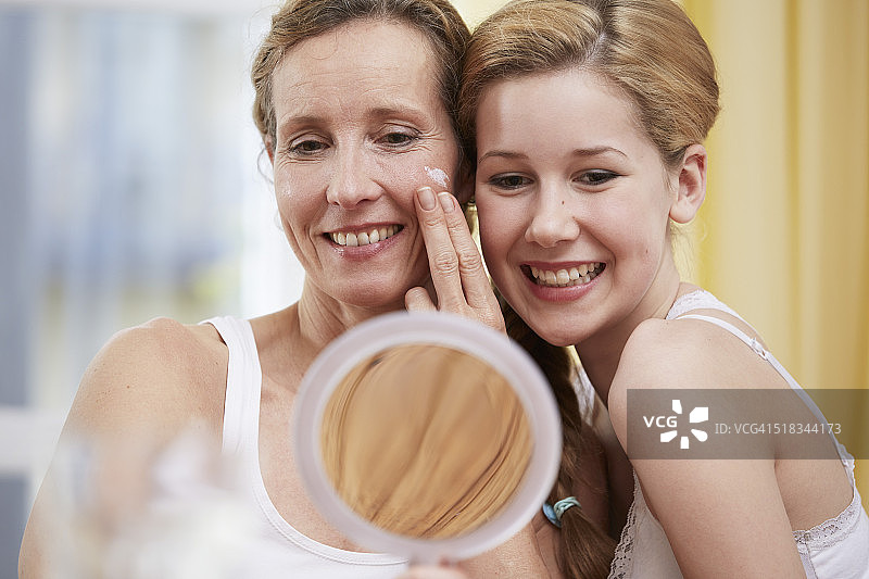 母亲和女儿的肖像用手持镜子加热到头部图片素材