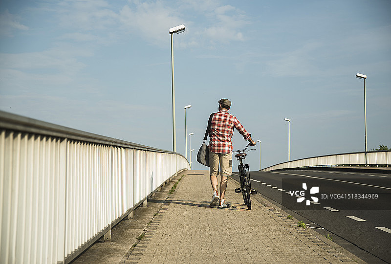 德国，曼海姆，戴帽子的男子推着自行车，后视图图片素材