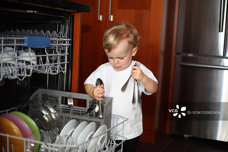 拿着餐具的小男孩在洗碗机旁边图片素材
