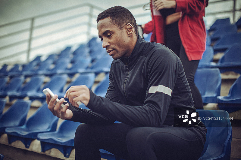 一名年轻的健康男子在剧烈运动后在体育场发短信图片素材