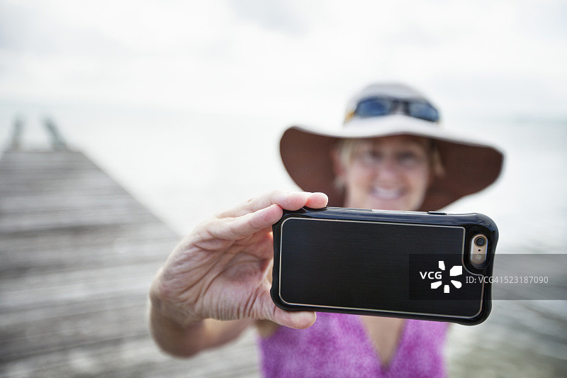 一名女子在伯利兹度假，用智能手机拍摄自己和海洋图片素材