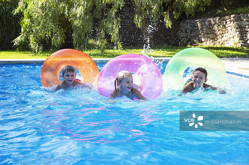 三个孩子在花园游泳池里玩充气环赛跑图片素材