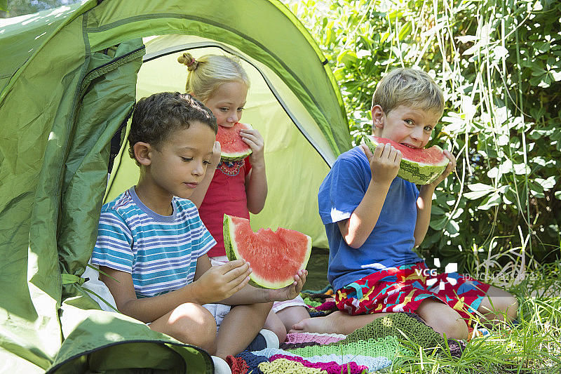 三个孩子在花园帐篷里吃西瓜片图片素材