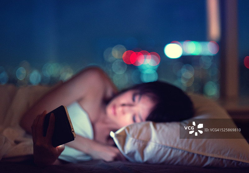 女人晚上在床上看智能手机图片素材