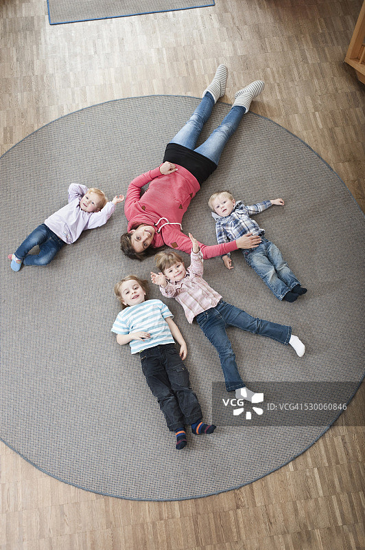 在幼儿园，女教育工作者和四个孩子在地上放松，高架视图图片素材