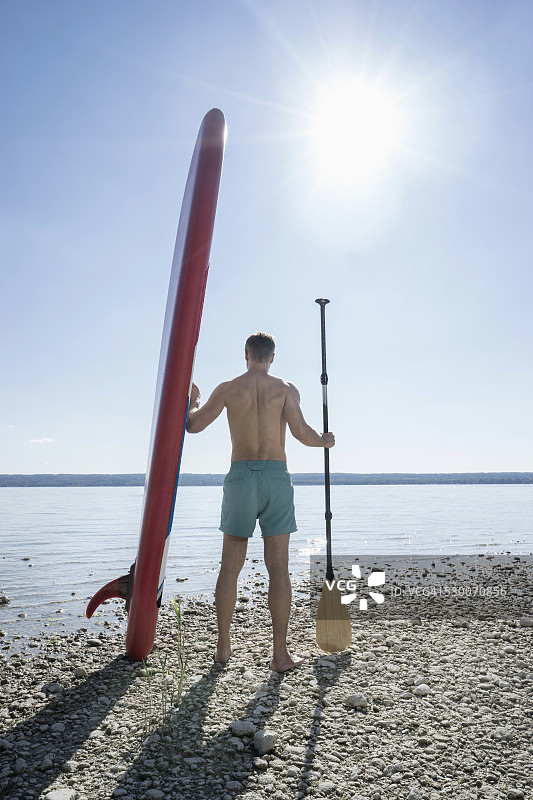 德国巴伐利亚，一名成年男子在湖边抬着冲浪板图片素材