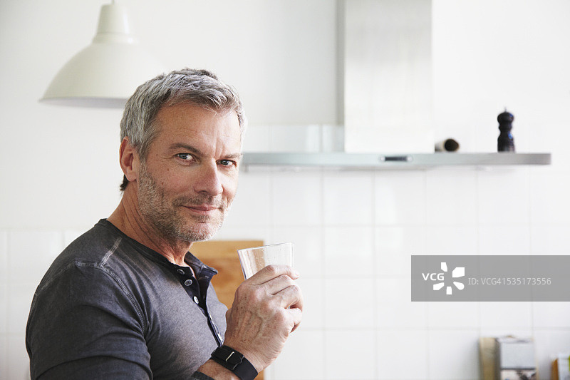 一个男人坐在厨房里，拿着一杯水图片素材
