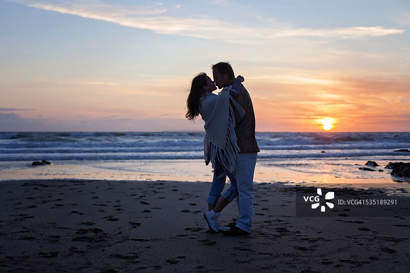 一对年轻的情侣在日落的海洋上相爱图片素材