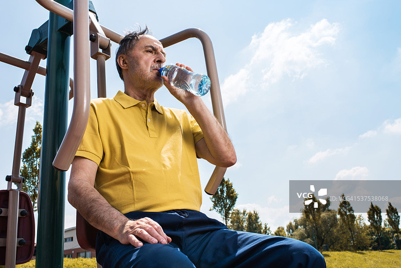 老人在户外机器上锻炼后喝水。图片素材