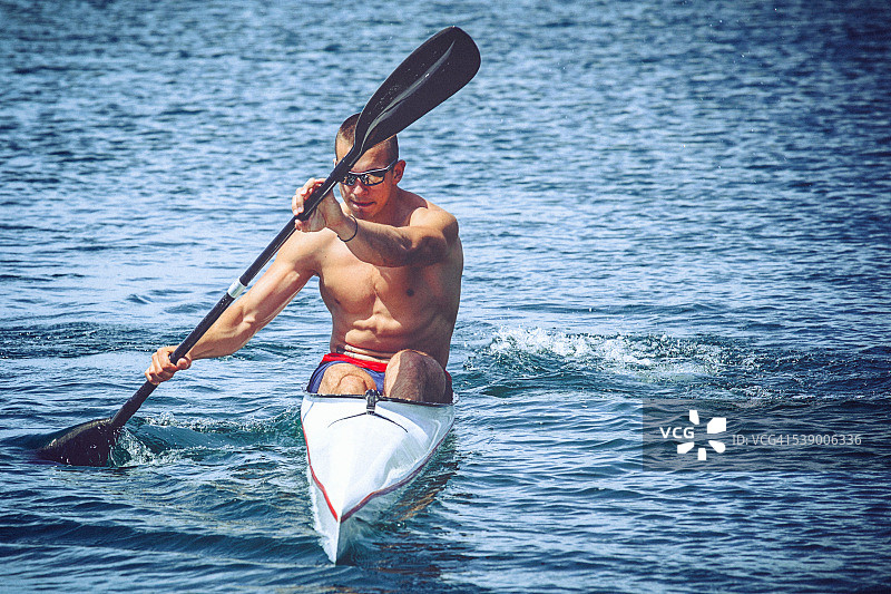 年轻的肌肉男子在皮划艇冲刺训练在静水。图片素材
