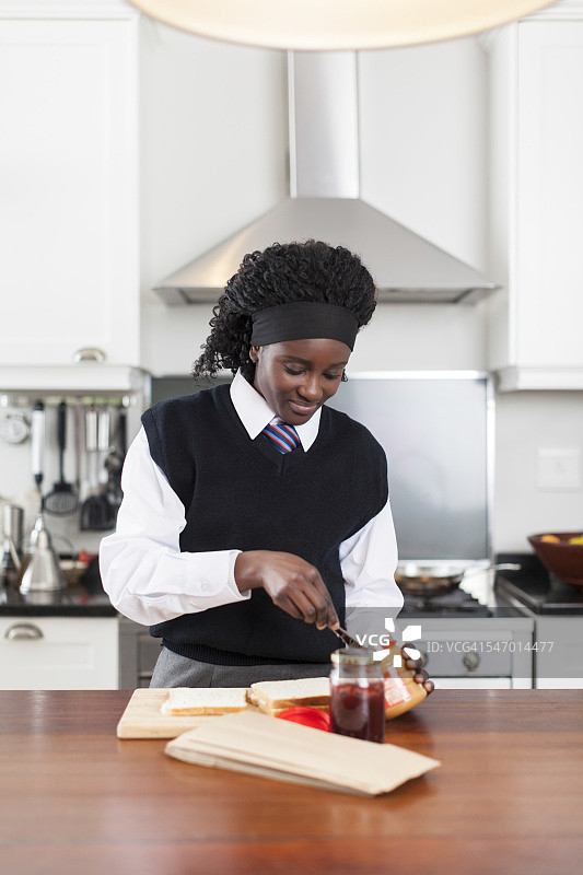 南非开普敦，一名非洲女学生正在为学校午餐制作花生酱和果冻三明治图片素材
