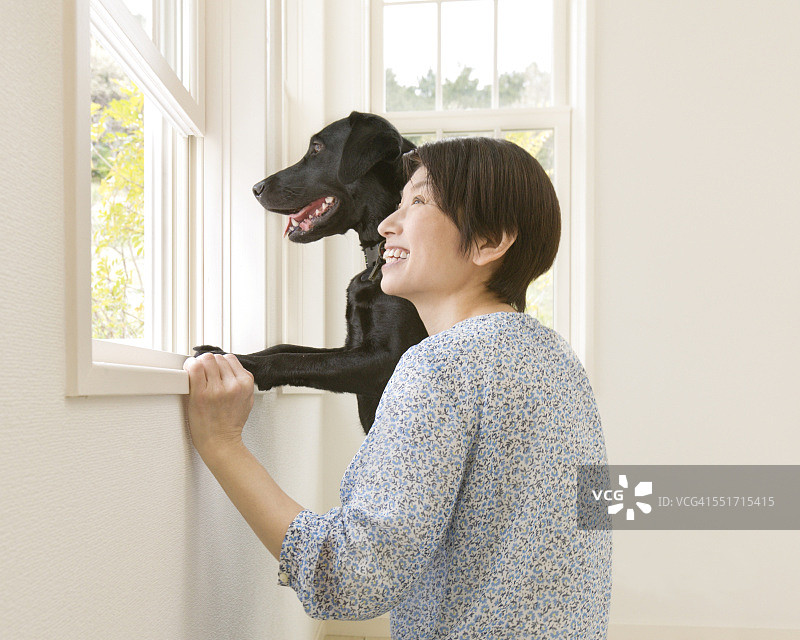 快乐的女人和她的狗透过窗户看图片素材