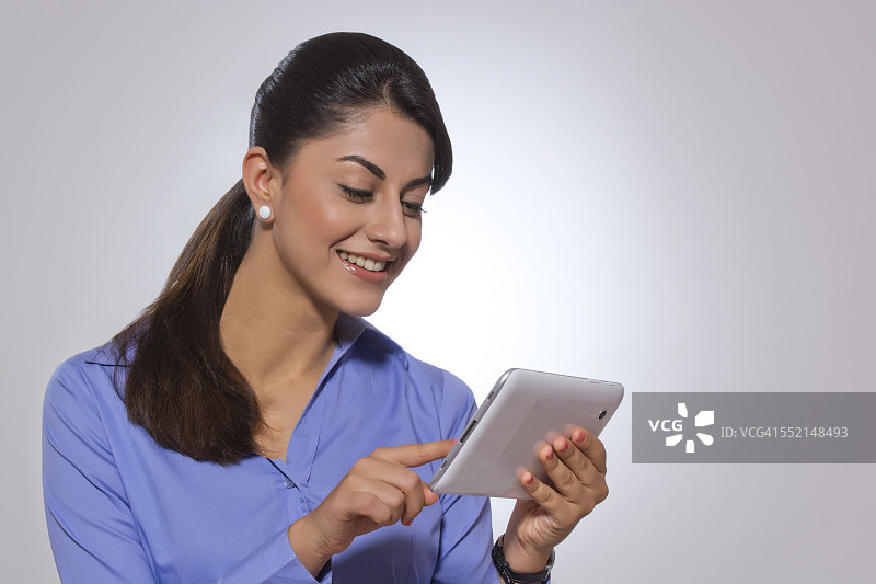 快乐的女商人在灰色背景下使用数码平板电脑图片素材