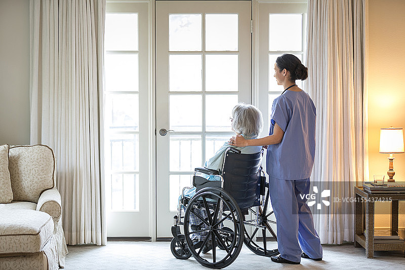 护士和年长病人坐在轮椅上，靠窗站着图片素材