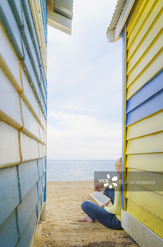 一个白人女人在五颜六色的海滩小屋外看书图片素材